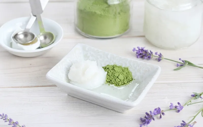 Primo piano di matcha in polvere su piattino bianco, ripreso da vicino per mostrarne consistenza, colore e forma su fondo chiaro o naturale.