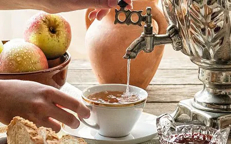 Détail des mains d’une personne préparant le thé avec un samovar métallique.