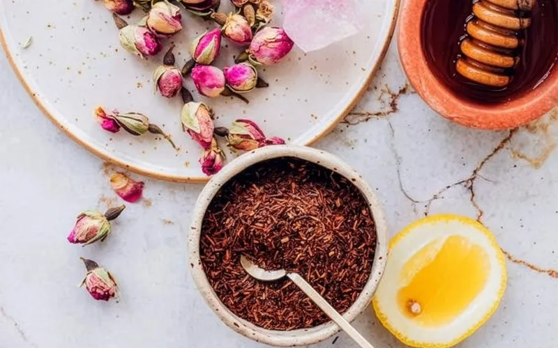 Inquadratura dall’alto di una composizione con petali di rosa, spezie, miele e ingredienti disposti ordinatamente su piano chiaro.