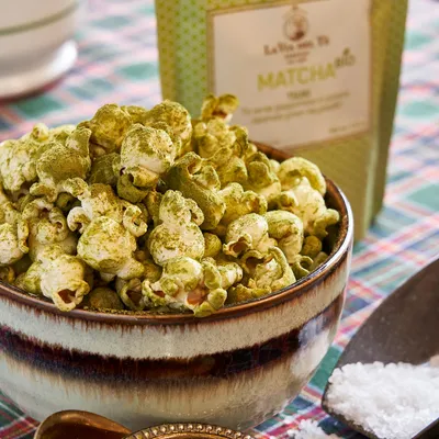 Primo piano di ciotola di popcorn verdi al matcha, impiattato con cura su un tavolo o sfondo neutro, con ingredienti e decorazioni visibili attorno.