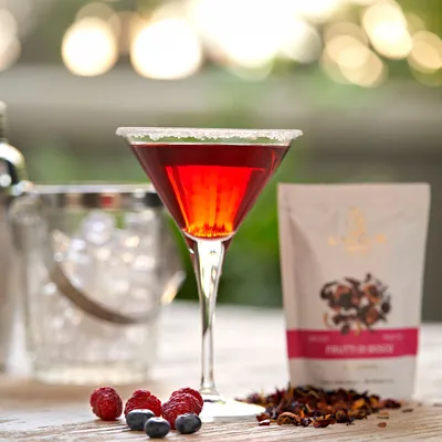 Primo piano di cocktail rosso con confezione e ingredienti, servito in un bicchiere o in una coppa con ingredienti decorativi e luce morbida.