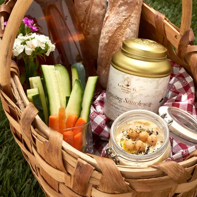 Cestino da picnic con gambi di sedano, un barattolo di prodotto e piccole ciotole con snack o salse.