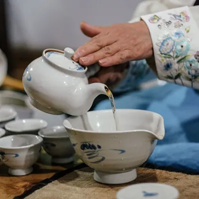 Person pours il tea from with teapot white into cups or bowls.