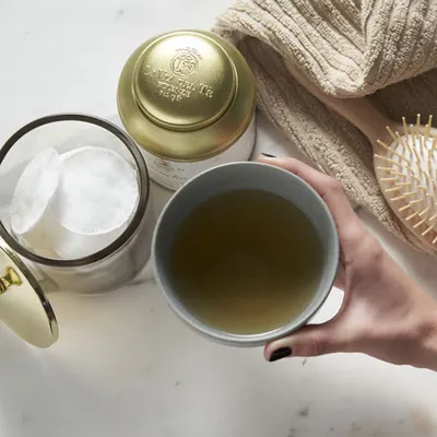 Détail d'une main qui verse il thé de un contenitore dans une tasse blanche.
