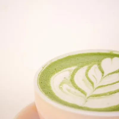 Matcha latte caldo in una tazza rosa, con schiuma di latte decorata a forma di foglia.