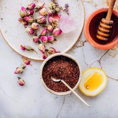 Inquadratura dall’alto di una composizione con petali di rosa, spezie, miele e ingredienti disposti ordinatamente su piano chiaro.