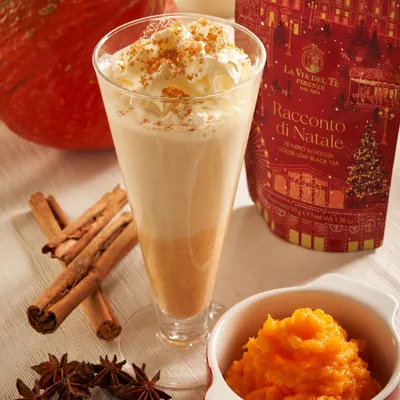 Bevanda tipo chai latte servita in un bicchiere alto, con spezie, scorza d’arancia e ingredienti appoggiati intorno.