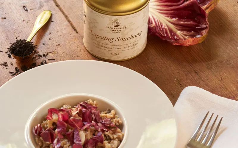 Primo piano di piatto gourmet con fiori e petali, impiattato con cura su un tavolo o sfondo neutro, con ingredienti e decorazioni visibili attorno.