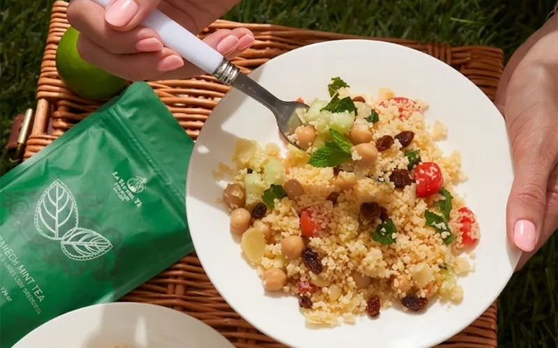 Scena di picnic all’aperto con picnic con piatto di pasta e borsa verde, piatti e accessori disposti su una tovaglia o sul prato.