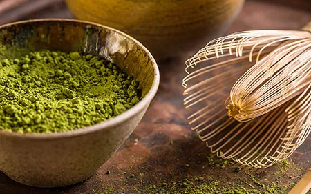 Ciotola with matcha green brillante and frusta of bambù appoggiata next to.