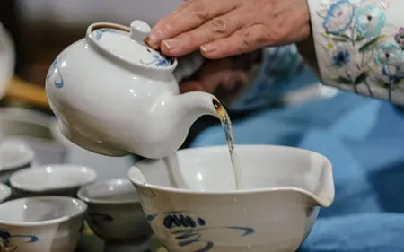 Personne versant le thé d’une théière blanche dans des tasses ou des bols.