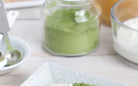 Primo piano di matcha in polvere su piattino bianco, ripreso da vicino per mostrarne consistenza, colore e forma su fondo chiaro o naturale.