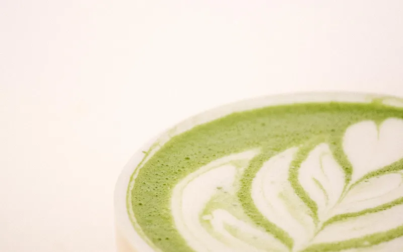 Hot matcha latte in a pink cup, with leaf-shaped latte art on the milk foam.
