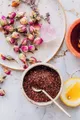 Inquadratura dall’alto di una composizione con petali di rosa, spezie, miele e ingredienti disposti ordinatamente su piano chiaro.