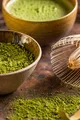 Ciotola con matcha verde brillante e frusta di bambù appoggiata accanto, fotografata in un set pulito e minimale.