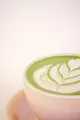 Matcha latte chaud dans une tasse rose, avec un motif de feuille dessiné dans la mousse de lait.