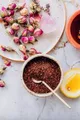 Inquadratura dall’alto di una composizione con petali di rosa, spezie, miele e ingredienti disposti ordinatamente su piano chiaro.