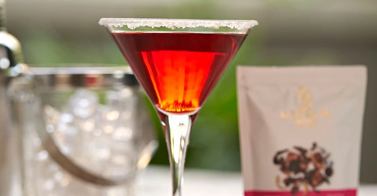 Close-up of red cocktail with package and ingredients.