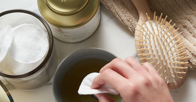 Détail d'une main qui verse il thé de un contenitore dans une tasse blanche.