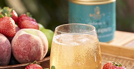 Bevanda alla frutta servita in un bicchiere, con barattolo di tè in primo piano e frutta fresca disposta intorno.