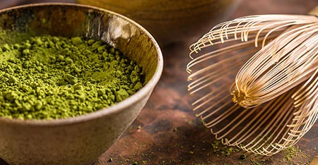 Ciotola with matcha green brillante and frusta of bambù appoggiata next to.