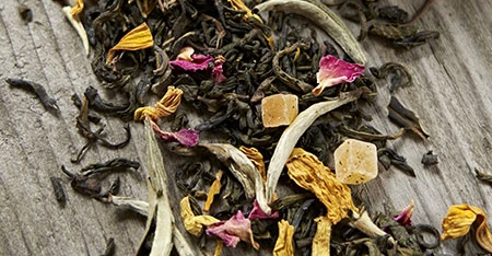 Primo piano di foglie di tè con petali colorati, ripreso da vicino per mostrarne consistenza, colore e forma su fondo chiaro o naturale.
