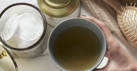 Détail d'une main qui verse il thé de un contenitore dans une tasse blanche.