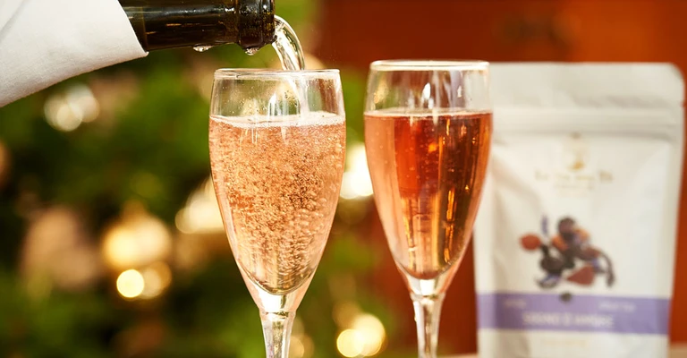 Due calici con bevanda chiara o rosata accanto a una confezione di tè, in una composizione elegante pensata per il brindisi.