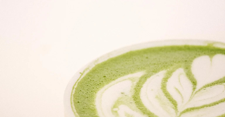 Matcha latte caldo in una tazza rosa, con schiuma di latte decorata a forma di foglia.