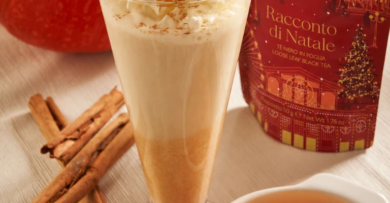 Bevanda tipo chai latte servita in un bicchiere alto, con spezie, scorza d’arancia e ingredienti appoggiati intorno.